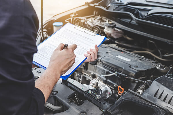 A person with a clipboard looking over a car engine